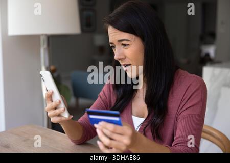 Woman looks concerned while holding credit card and smartphone Stock Photo