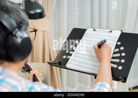 Rear view shot of a man wearing glasses practices guitar in a studio. Selective focus on hand. Creativity, and artistry involved in music-making. Stock Photo