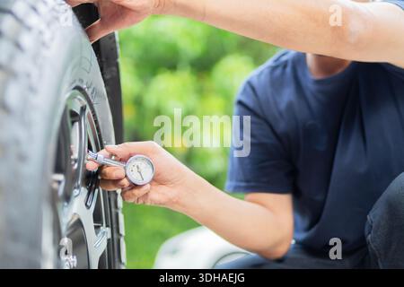 Man checking status of car's tires by car tire pressure sitting over nature background. Selective focus. Stock Photo