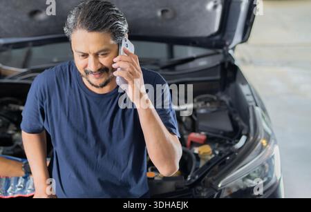 Mechanical fixing car at home. Repairing Service advice by mobile phone. High angle view shot, portrait. Stock Photo