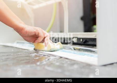 Woman hand cleaning a dirty and dusty air conditioning filter with a sponge and liquid in her house. Selective focus. Stock Photo