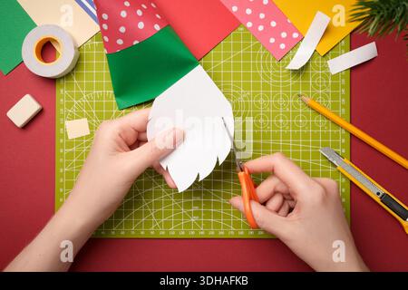Making a gnome craft. Hands cut out a beard from white paper. Creative process. Stock Photo