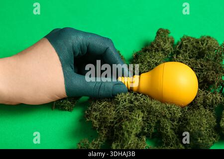 Human hand with painted fingers, light bulb and moss on green background. Concept of green technology Stock Photo