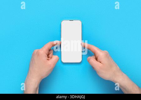 Male hands pointing at blank mobile phone on blue background. Medicine concept Stock Photo
