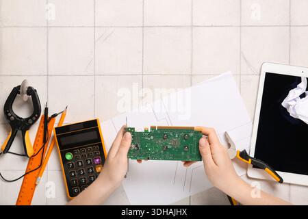 Young woman with video card, crumpled paper, schematics and calculator on table. Inventor concept Stock Photo