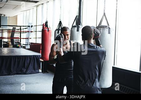 Man, boxing and fitness with personal trainer at gym for training, punching technique and combat. Male boxer, coaching and sports mitts for self Stock Photo