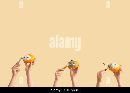 Female hands holding pumpkins with drawn faces and clay masks on beige background Stock Photo