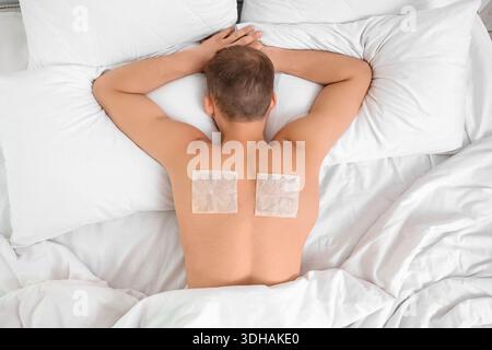 Young man with mustard plasters on his back lying in bedroom, top view Stock Photo