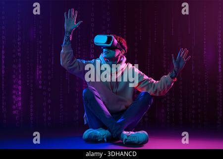Young man using VR glasses on dark background with digital code Stock Photo