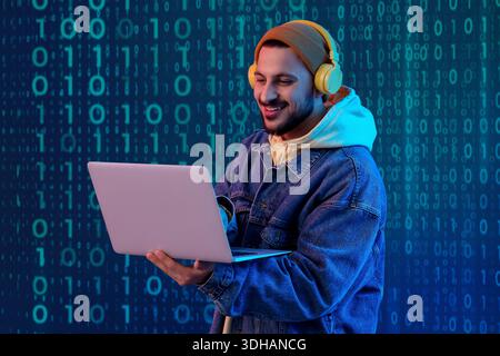 Young male programmer in headphones using laptop on dark color background Stock Photo
