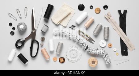 Thread spools with fabric, measuring tape, scissors and sewing supplies on grey background Stock Photo