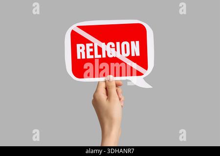 Hand holding speech bubble with crossed-out word RELIGION on grey background. Atheism concept Stock Photo