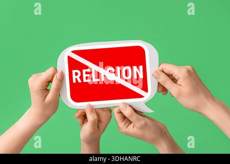 Hands holding speech bubble with crossed-out word RELIGION on green background. Atheism concept Stock Photo