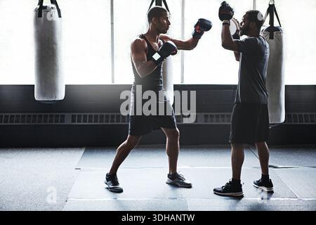 Athlete, people and boxing with personal trainer at gym for training, punch technique and combat. Boxer, fitness coach and sports mitts for self Stock Photo