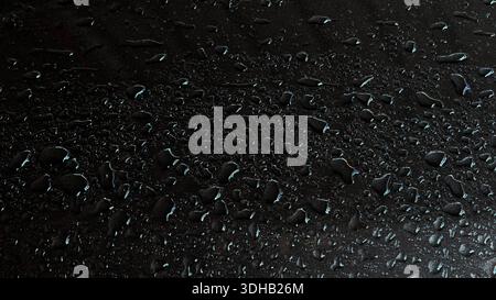 Sleek close-up shot of shimmering water droplets on dark textured metallic surface. Features moody lighting with subtle blue and gold reflections perf Stock Photo