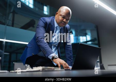 Focused black mature businessman leaning over conference table while working on laptop Stock Photo