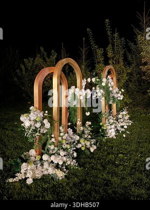 Elegant outdoor wedding ceremony setup featuring golden metal arches decorated with white flowers and greenery on a lawn Stock Photo