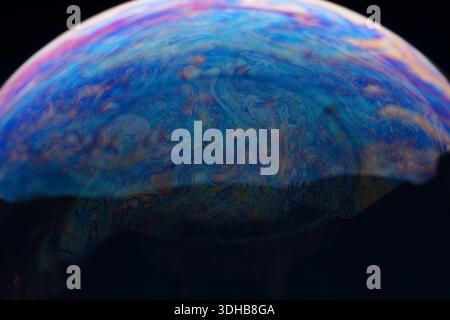 Close-up of a soap bubble with vibrant, swirling patterns and colors on a dark background, ideal for creative concepts and backgrounds. Stock Photo