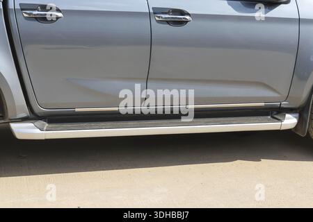 Side view grey pickup truck showing robust metal running board step bar attached under door for easy access into vehicle cabin illustrating sturdy chr Stock Photo