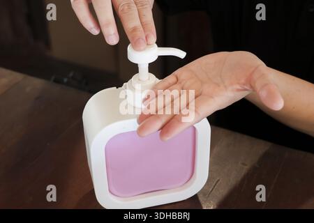 Hygiene concept showing person hand pumping liquid soap from dispenser bottle on wooden table for cleaning and washing to protect against virus infect Stock Photo
