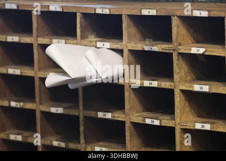 Old vintage wooden sorting rack with empty slots and single compartment containing white folded paper showing abandoned mail concept in rustic post of Stock Photo