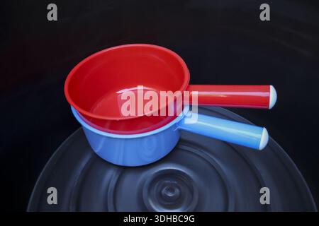 Close up view of bright red and light blue plastic water dipper stacked together dark ribbed background showing utilitarian simplicity and domestic or Stock Photo
