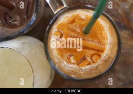 Top view glass of refreshing sweet Thai iced tea with milk orange beverage cold drink on wooden table summer refreshment traditional asian creamy tast Stock Photo