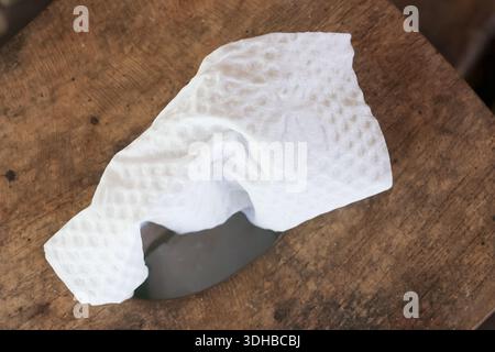 Crumpled white cleaning wipe with textured surface lying on dark weathered wooden table background showing contrast between clean hygiene supply and r Stock Photo