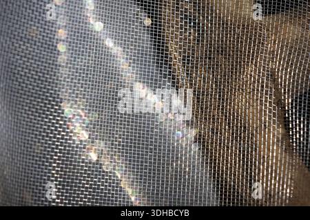 Abstract mesh screen texture with sunlight reflection creating moody atmosphere and obscure shadow behind dark gray mosquito net surface pattern Stock Photo