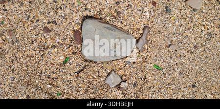 Close-up of a gray stone lying on a bed of coarse sand mixed with small shells and pieces of green glass Stock Photo