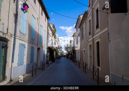 Unknown location - April 2, 2023: A narrow street lined with residential buildings featuring pastel facades and closed shutters, with overhead wires and decorative street lamps, under a blue sky with scattered clouds. Stock Photo