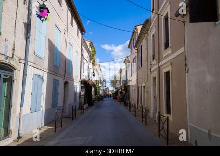 Unknown location - April 2, 2023: A narrow street lined with residential buildings featuring pastel facades and closed shutters, with overhead wires and a decorative street lamp, under a blue sky with scattered clouds. Stock Photo