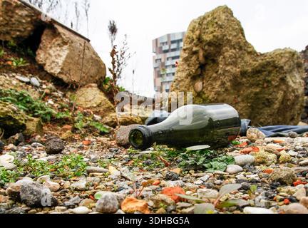 empty glass bottle abandoned among urban ruins and rubble. The image highlights pollution and environmental degradation near a modern city. Concept of Stock Photo