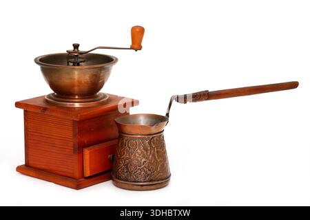 On a white background, an old wooden hand-cranked coffee grinder next to a copper coffee pot Stock Photo