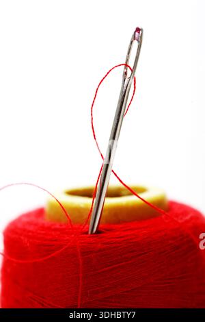 Very close-up. A sewing needle is stuck in a spool of red thread Stock Photo