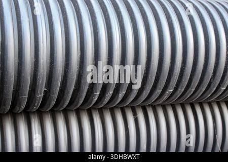 Notably corrugated and ribbed texture of the pipes. A close-up of several stacks of black, ribbed, double-wall corrugated plastic pipes. Stock Photo