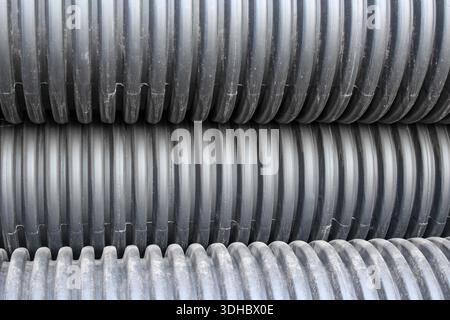 Notably corrugated and ribbed texture of the pipes. A close-up of several stacks of black, ribbed, double-wall corrugated plastic pipes. Stock Photo