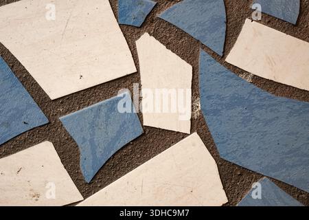 Close-up of irregular blue and white ceramic tiles arranged on dark grout, forming a textured mosaic surface. Stock Photo