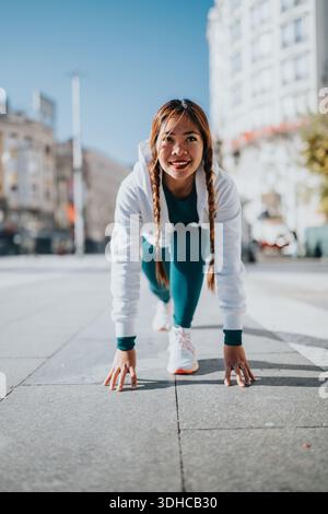 Athletic woman in teal leggings on a busy city street performing a stretching warm-up pose Stock Photo