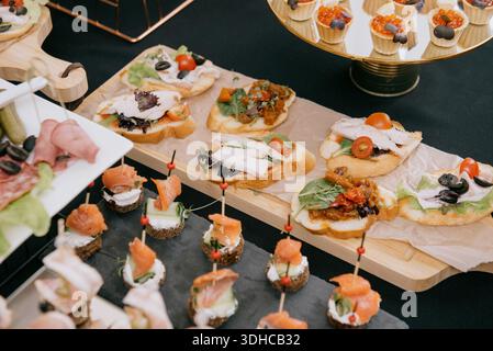Assorted bruschetta with chicken and vegetables next to salmon canapes. Assorted cold appetizers on wooden boards and slate trays for restaurant cater Stock Photo