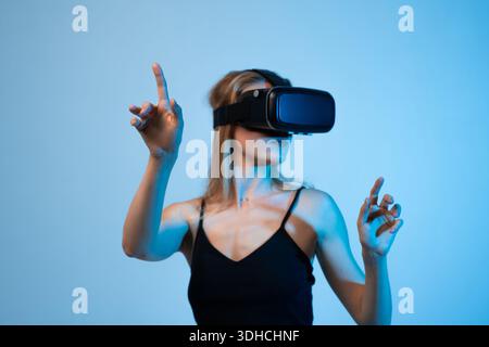 Woman using virtual reality headset and pointing at virtual interface, immersive metaverse experience and future technology Stock Photo