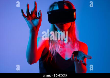 Close up of woman interacting with virtual interface using hands and VR headset, immersive futuristic technology concept with neon lighting Stock Photo