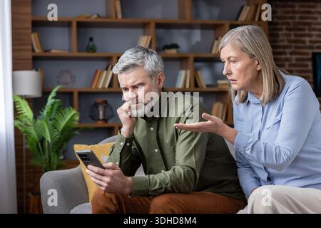 Mature couple having a disagreement while the man is distracted by his smartphone, highlighting issues of neglect and communication problems in their relationship at home Stock Photo