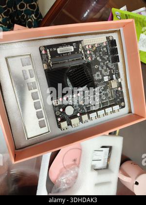 Open computer motherboard with cooling fan in pink box, displayed on desk with accessories Stock Photo