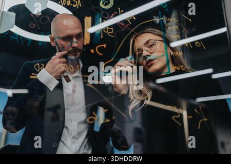 Business professionals collaborate on a glass board with equations during a high-level brainstorming session Stock Photo