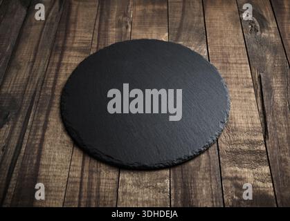 Blank black round slate plate on wooden surface. Copy space. Stock Photo