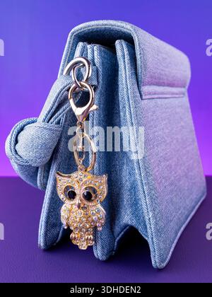 A close-up of a metal keychain in the shape of an owl adorned with white rhinestones on  blue bag Stock Photo