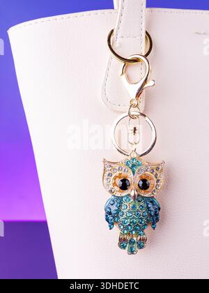 A close-up of a metal keychain in the shape of an owl adorned with blue rhinestones on  white bag Stock Photo