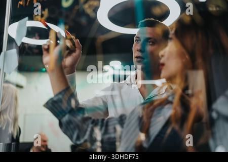 Business team brainstorms at glass board in modern office during a collaborative meeting Stock Photo