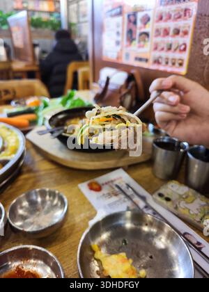 Hand Holding Korean BBQ Dish with Vegetables and Meat at Restaurant Table Stock Photo